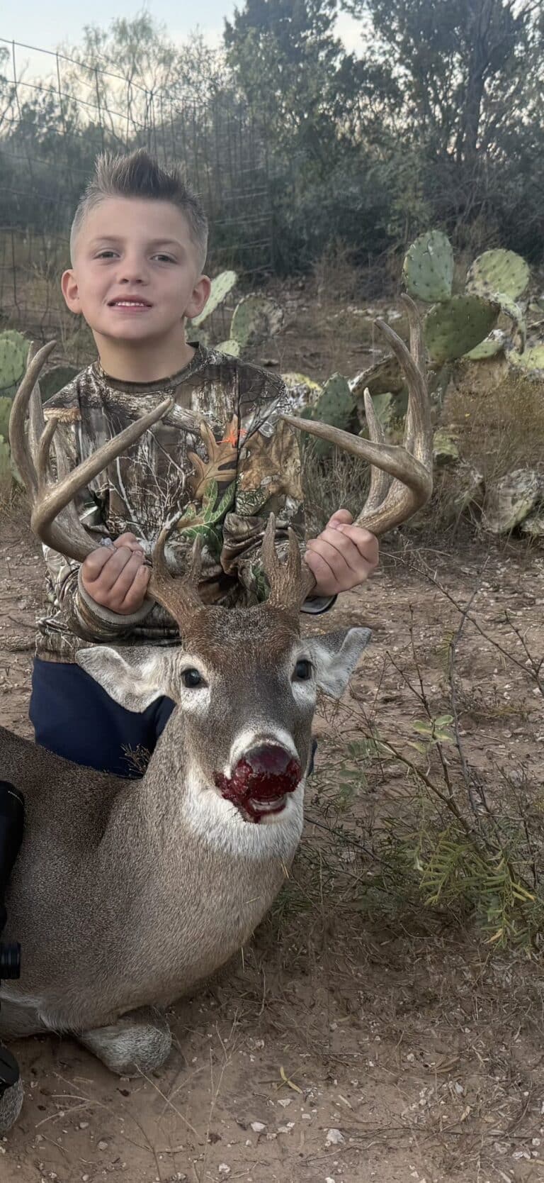 Young hunter holding the antlers of his whitetail buck beside prickly pear cactus